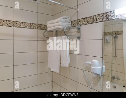 Handtücher auf einem Handtuchhalter aus Edelstahl in einem Hotelbadezimmer mit großen hellen Keramikfliesen, modernes, sauberes Design Stockfoto