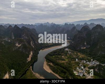 Aus der Vogelperspektive auf den Li-Fluss, der sich durch Karstberge schlängelt, eine Sinfonie aus Smaragd und Grau unter einem bewölkten Himmel, Xingping, China. Stockfoto