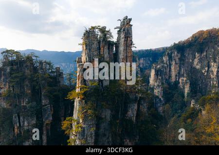 Aus der Vogelperspektive ziehen zerklüftete Gipfel in den Himmel, umhüllt von grünem Laub, eine Symphonie von Erdtönen, die sich nahtlos mit dem Himmel verschmelzen, Zhangjiajie Stockfoto