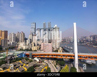 Blick aus der Vogelperspektive auf eine Skyline, unterbrochen von dem berühmten Raffles City Chongqing Komplex und der dynamischen orangen Brücke, die im Kontrast zum ruhigen Fluss CH steht Stockfoto