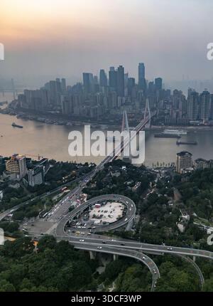 Die Skyline der Stadt steht im Kontrast zu einem Fluss, der von einer modernen Brücke überquert wird: Chongqing, Chongqing, China. Stockfoto