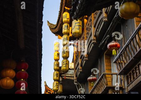 Blick auf leuchtende Laternen, die an kunstvoll verzierten Holzkonstruktionen hängen und ein warmes Licht auf die Straße werfen, Furong Town, Hunan, China. Stockfoto
