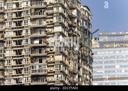 Blick auf ein hohes, älteres Wohngebäude mit vielen Fenstern und Klimaanlage neben einem modernen Glasgebäude, Chongqing, Chongqing, China. Stockfoto