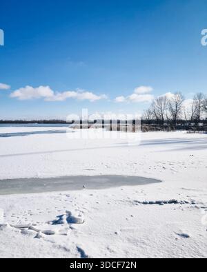 Ruhige Winterlandschaft eines gefrorenen Sees unter einem klaren blauen Himmel. Riesiger, schneebedeckter gefrorener See an einem hellen, sonnigen Tag. Stockfoto