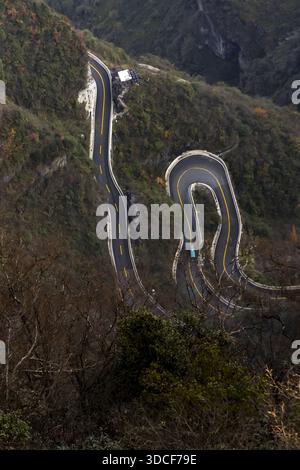 Der Blick auf eine gewundene Straße schlängelt sich durch das üppige, bergige Gelände, die scharfen Kurven, die einen Pfad inmitten von lebhaftem Grün, Zhangjiajie, Hunan und Chin bilden Stockfoto