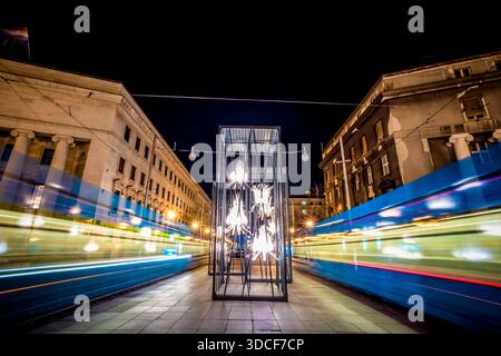Zagreb, Kroatien - 16. März 2023: Blick auf pulsierende Straßenbahnen, die an einer beleuchteten Kunstinstallation vorbeiziehen, im Kontrast zur dunklen Nacht und Klassik Stockfoto