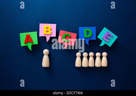 Holzfiguren, die mit Sprechblasen interagieren, zeigen bunte Buchstaben auf dunklem Hintergrund Stockfoto