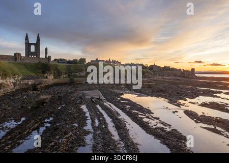 Aus der Vogelperspektive der dramatischen Ruinen der St. Andrews Cathedral stehen Sie stolz vor dem feurigen Sonnenuntergangshimmel und werfen lange Schatten über die zerklüftete Küste. Stockfoto