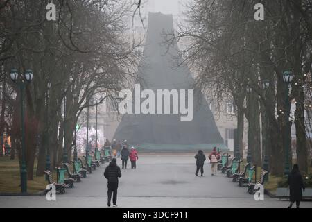 Die Menschen laufen entlang einer Gasse, die zum Taras Schewtschenko-Denkmal führt, das vor möglichen Schäden durch russische Bombenangriffe abgeriegelt ist, im Taras Schewtschenko-Garten im Nebel, Charkiw, Ukraine, 20. Dezember 2025. (Foto: Viacheslav Madiievskyi/Ukrinform) Stockfoto