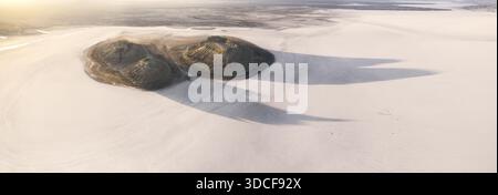 Aus der Vogelperspektive werfen lange Schatten über eine weite, helle Weite, deren dunkle Formen sich in starkem Kontrast zur umgebenden gebleichten Landschaft bilden Stockfoto