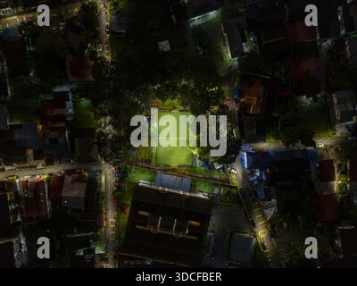 Aus der Vogelperspektive auf das hell beleuchtete grüne Feld, umgeben von Gebäuden und Bäumen, ein starker Kontrast zur Dunkelheit, Kuala Lumpur, Malaysia. Stockfoto