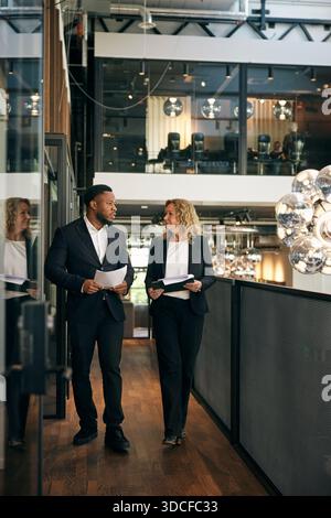 Rechtsexperten, die Dokumente halten, die miteinander reden, während sie im Bürokorridor laufen Stockfoto