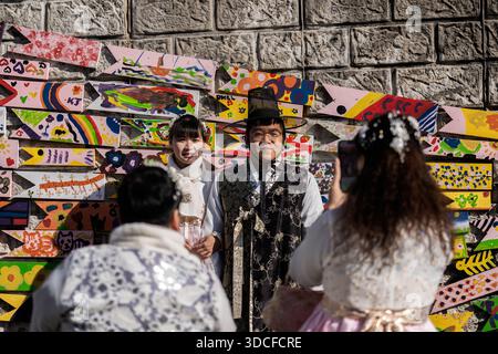 Busan, Südkorea - 15. Dezember 2025: Blick auf ein Paar in traditioneller koreanischer Kleidung, das sich vor einer lebendigen, mit Graffiti geschmückten Steinmauer, einer Fotogra, posiert Stockfoto