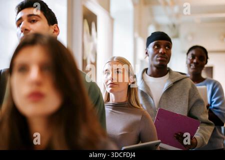 Nachdenkliche junge Frau wartet in Schlange mit Freunden auf dem Universitätscampus Stockfoto