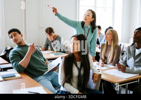Eine Professorin zeigt, während sie Studenten unterrichtete, die am Schreibtisch im Klassenzimmer sitzen Stockfoto