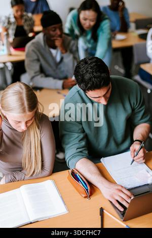 Hochwinkelansicht fokussierter männlicher und weiblicher Freunde, die im Klassenzimmer am College studieren Stockfoto