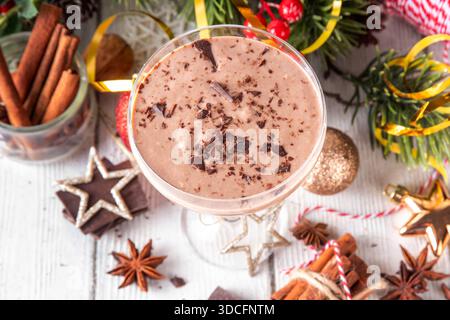 Gewürzter Schokoladen-Eierlikör-Martini-Cocktail, serviert mit Zimtstab, Muskatnuss und Schokolade, auf gemütlichem Weihnachtshintergrund Stockfoto