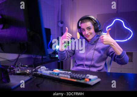 Ein fokussierter Gamer sitzt am Schreibtisch und tippt auf einer mechanischen Tastatur in einem neonbeleuchteten Gaming-Setup. Wenn sie ein Headset um den Hals tragen, sehen sie selbstbewusst aus, während sie sich an einem PC-Gaming oder Streaming-Aktivitäten beteiligen || Modell veröffentlicht Stockfoto
