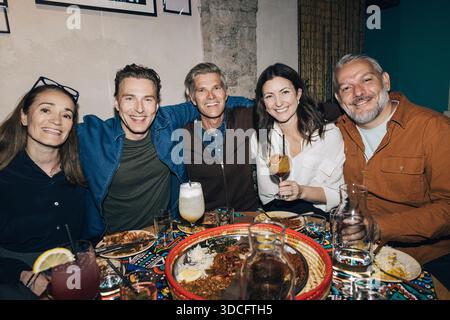 Eine Gruppe männlicher und weiblicher Freunde sitzt mit Armen im Restaurant Stockfoto