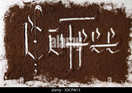 Kalligraphische Inschrift gotischen Buchstaben Kaffee über Grund schwarzer Kaffee verstreut auf weißem Marmor. Kaffee trinken Konzept Hintergrund. Ansicht von oben Stockfoto