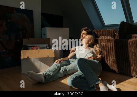 Sonnenlicht scheint auf junge Frau, die Freizeit mit ihrem Freund verbringt, während sie in der Nähe von Kartonschachteln in der Wohnung sitzt Stockfoto