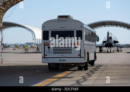 Moron, Spanien - 12. Mai 23: Ein weißer Schulbus parkt auf einem Flugplatz mit Flugzeughangars im Hintergrund Stockfoto