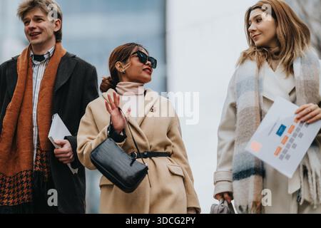 Drei stilvolle Geschäftsleute spazieren zusammen in Winterkleidung durch die Stadt und teilen sich einen freundlichen Moment Stockfoto