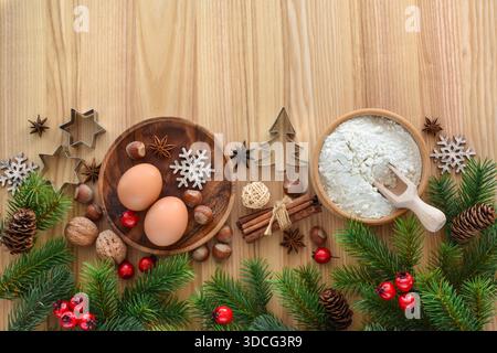 Vorbereitung zum Feiertagsbacken mit Eiern, Mehl, Nüssen und Fichtenzweigen auf einem Holztisch. Draufsicht. Mit Platz für Ihren Text Stockfoto