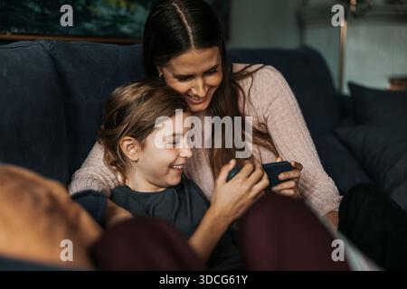 Lächelnde Mutter und Tochter, die zu Hause auf dem Smartphone Videos anschauen Stockfoto