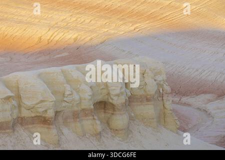 Blick auf scharf weiße und rote Felsformationen unter einem Himmel aus weichem Pfirsich und Orange, strukturiert und gestreift, in Senek, Region Mangystau, Kasachstan. Stockfoto