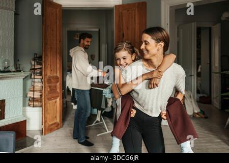 Lächelnde Mutter, die ihre Tochter zu Hause mit dem Huckepack versorgt Stockfoto