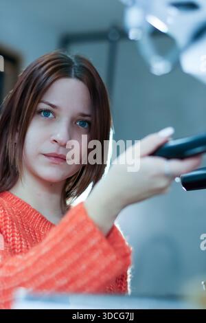 Porträt der brünetten Frau im Strickpullover, der Kaffeemaschinenteil mit ernstem Ausdruck in Innenräumen behandelt. Stockfoto