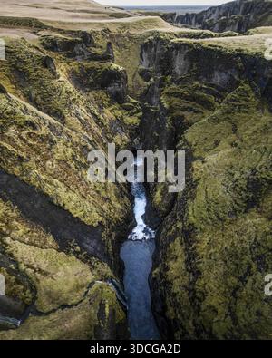 Aus der Vogelperspektive auf eine tiefe Schlucht, die von einem Fluss gemeißelt wurde und die Strukturen von moosbedeckten Klippen und den starken Kontrast von Wasser und Stein, Vik, Western R, enthüllt Stockfoto