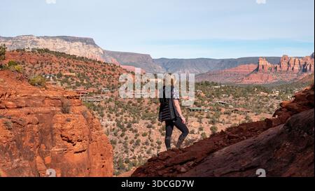 Blick auf eine Frau, die auf roten Felsen steht und das weitläufige Tal und die weit entfernten Mesas unter klarem Himmel in der Arizona-Wüste, Arizona, USA, bestaunt. Stockfoto