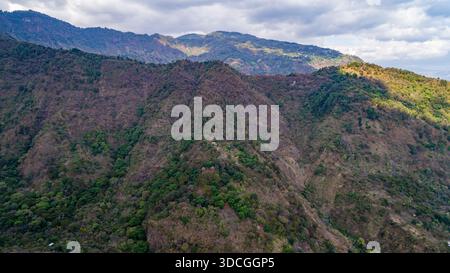 Aus der Vogelperspektive auf zerklüftete, grüne Berge, die unter einem fleckigen Himmel kaskadieren, San Marcos La Laguna, Departement Sololá, Guatemala. Stockfoto
