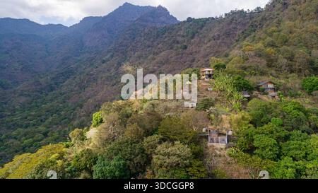 Blick aus der Vogelperspektive auf rustikale Wohnungen eingebettet zwischen den üppigen, grünen Hängen unter dem wachsamen Blick auf den majestätischen Berggipfel, Lake Atitlan, Sololá D Stockfoto