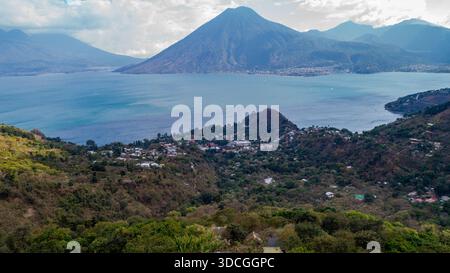 Aus der Vogelperspektive auf den majestätischen Atitlan-See, umgeben von grünen Hügeln, mit dem imposanten Kegel eines Vulkans, der am Horizont durchdringt, San Marcos La Laguna, so Stockfoto