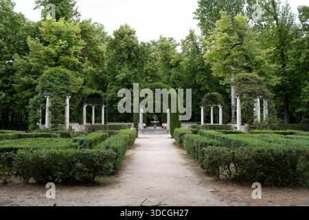 Ein ruhiger Gartenweg, gesäumt von ordentlich geschnittenen Hecken und Bäumen, mit klassischen Säulen und einem grünen Bogengang, schafft eine ruhige Atmosphäre Stockfoto