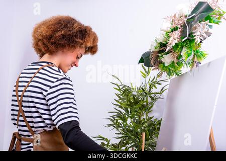 Junger Künstler lächelt, während er in einem hellen Atelier an einer leeren Leinwand arbeitet Stockfoto