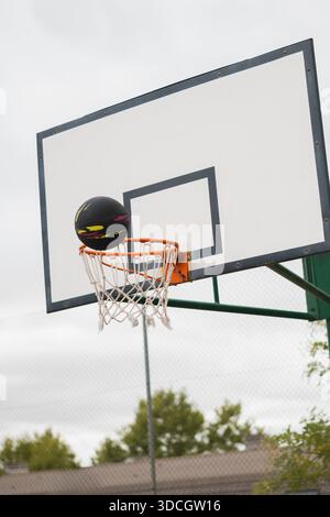 Basketball fällt durch ein Netz auf einem Platz im Freien mit einem Rückenbrett vor einem bewölkten Himmel Stockfoto
