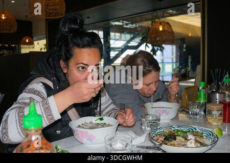 Zwei Frauen genießen traditionelle vietnamesische Pho-Suppe in einem modernen Restaurant Stockfoto