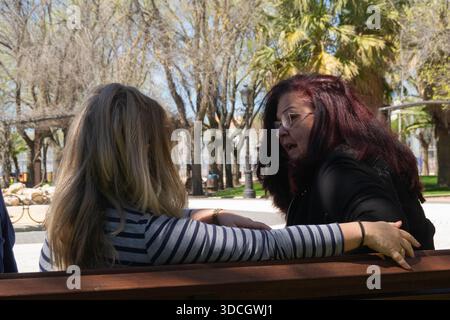 Zwei Frauen sitzen auf einer Bank im Park, reden und Gesten Stockfoto