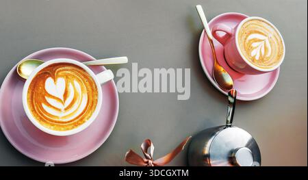 Zwei Tassen Cappuccino mit blumenförmiger Latte Art auf rosafarbenen Untertassen auf einem Tisch. Draufsicht Stockfoto