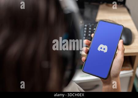Ein nicht erkennbarer weiblicher Teenager hält ein Mobiltelefon mit dem Discord-Logo auf dem Bildschirm mit blauem Hintergrund Stockfoto