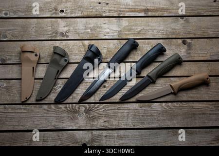 Satz taktischer Überlebensmesser und Hüllen in verschiedenen Farben auf einer Holzoberfläche. Stockfoto