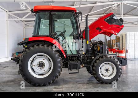 Moderner roter Traktor mit offener Motorhaube in der Servicegarage, Inspektion von Landmaschinen, Wartung von Landfahrzeugen, Reparatur schwerer Geräte, technisches Konzept für den ländlichen Raum. Stockfoto
