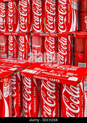 Liepaja, Lettland- 12. Dezember 2025: Gestapelte Coca-Cola Original Geschmacksdosen und Multipacks in einem Ladenregal mit Branding und Einzelhandelspräsentation. Stockfoto