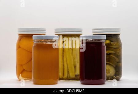 Eine Sammlung von Glasgläsern, die mit verschiedenen konservierten Lebensmitteln gefüllt sind, befindet sich auf einer glatten weißen Oberfläche. Stockfoto