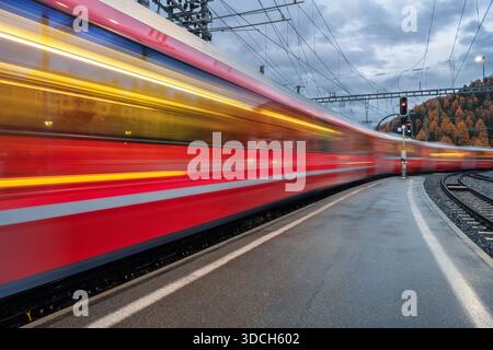 Verschwommener roter Personenzug, der am Bergbahnhof vorbeifährt Stockfoto