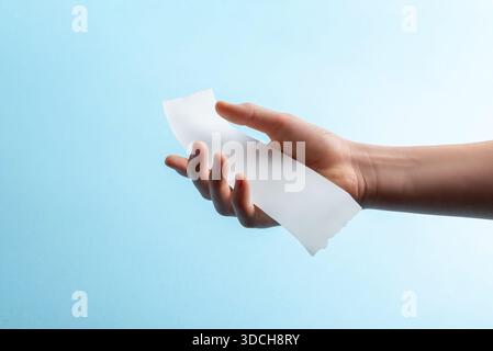 Hand mit gekrümmtem, leerem Papierbeleg auf blauem Hintergrund, minimalistisches Finanzmodell für Spesendokumente, Rechnungsvorlagen und Design-Präsentationen Stockfoto